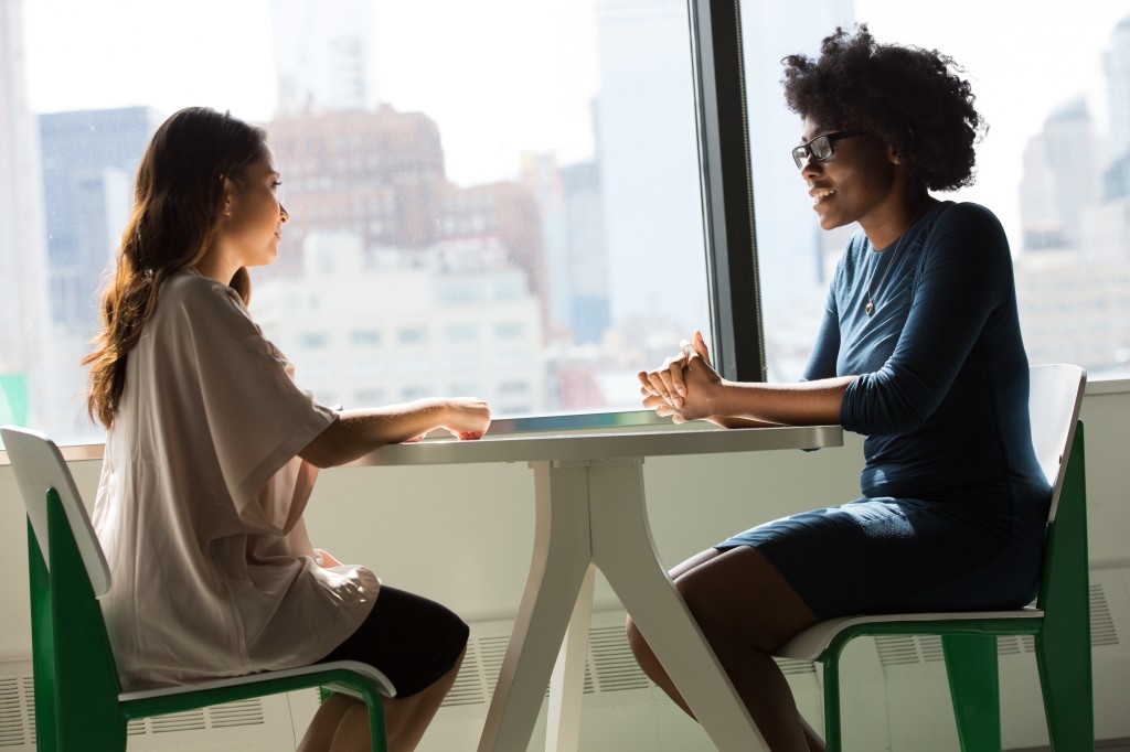 Photo de deux femmes en train de parler ensemble pour illustrer cet article sur la question "Parlez-moi de vous" posée en entretien d'embauche